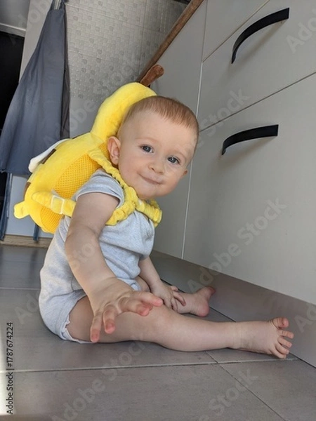 Fototapeta A six-month-old baby sits with a supportive bee-shaped pillow, ensuring safe practice of sitting skills.

