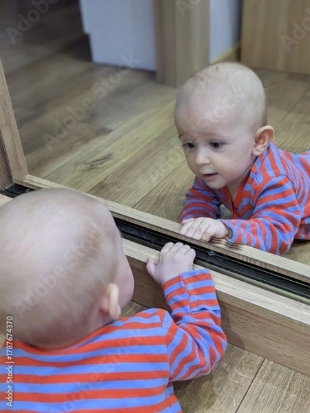 Fototapeta A curious baby lying on his tummy, fascinated by his own reflection in a mirror.

