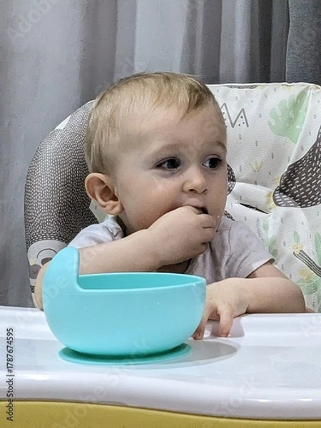 Fototapeta A joyful baby happily eating finger food by himself, exploring tastes and textures.

