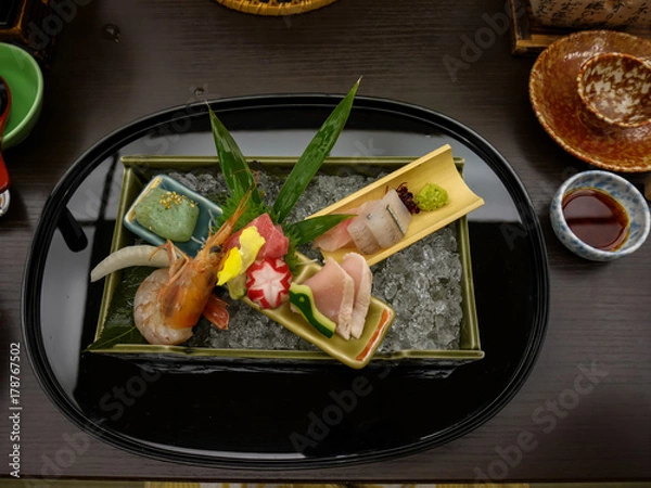 Obraz Japanese ryokan kaiseki dinner decorative sashimi set including Pacific blue fin tuna, shrimp, greater amberjack, halfbeak, konjac in ooishi on crushed ice tray with wasabi and soy sauce