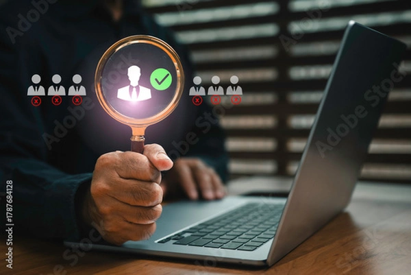Fototapeta Businessman using magnifying glass to choose the right candidate on laptop, symbolizing recruitment, human resources management, employee selection, and hiring process in modern business.
