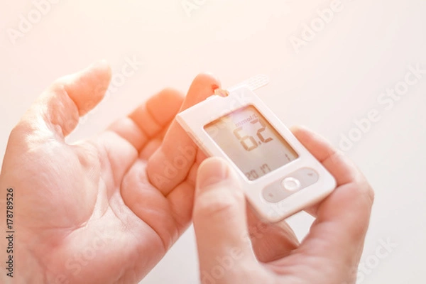 Fototapeta Medicine, diabetes, glycemia, health care and people concept - Close up of man hands testing high blood sugar level with glucometer or glucose meter and test stripe at home