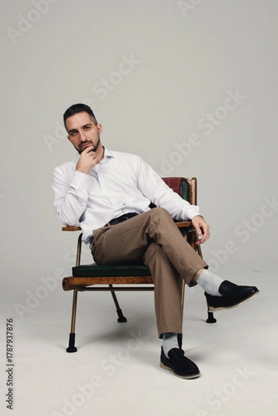 Fototapeta A man sitting on a chair against a white background. Male portrait.
