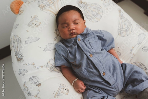 Fototapeta Cute newborn baby boy sleeping peacefully in white crib and soft nest. Close-up of infant resting on bed, symbolizing childhood innocence, comfort, and family love. Perfect for baby care themes.