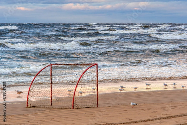 Fototapeta Seagulls gather near a beach soccer goal at sunset with crashing waves in the background
