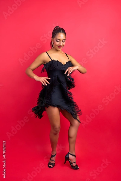 Fototapeta Woman enjoying a lively salsa dance in a black fringe dress on a red background