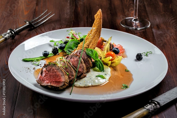 Obraz Delicious medium rare meat steak with sauce and salad on a plate. Healthy food made of meat fillet with fresh herbs and wine on a wooden table.