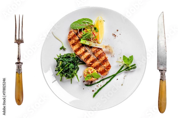 Obraz Plate with delicious grilled salmon fish steak and salad isolated on white background. Healthy food made of fish and vegetables. Top view.