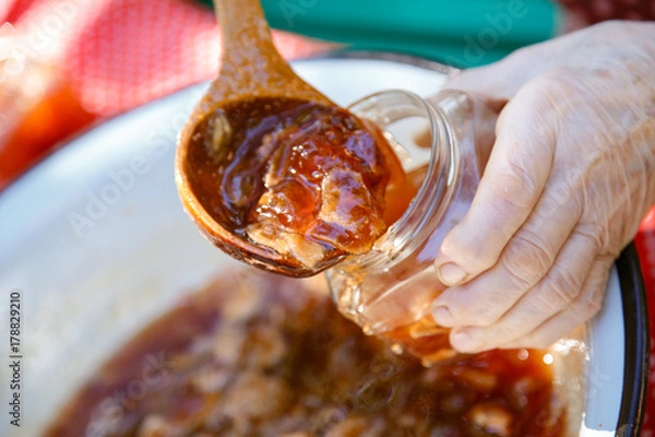 Fototapeta Hands pour jam from apples into jars. The process of preparing jam. Jam from apples.