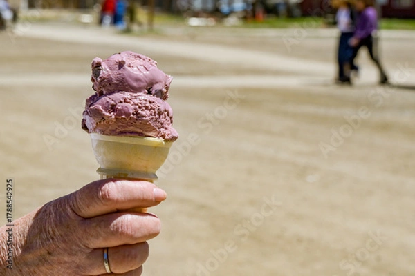 Obraz Close up view of a person outdoors, holding a cone with cherry ice cream