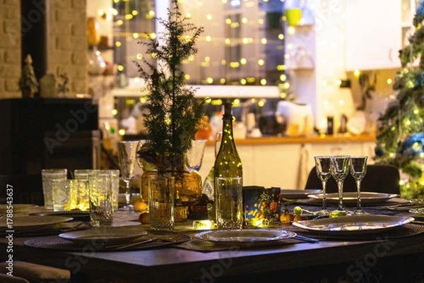 Fototapeta A festive table set for guests for Christmas and New Year, a Christmas tree in the living room, plates, bottles, glasses, potted plants, fairy lights