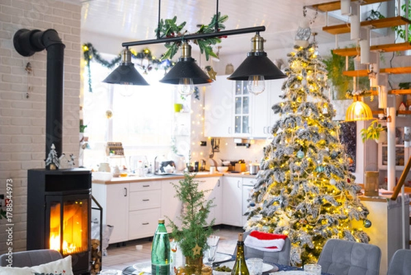 Fototapeta Festive interior of house is decorated for Christmas and New Year in loft style with black stove, fireplace, Christmas tree. Warm studio room with set table, burning wood, cozy and heating of home