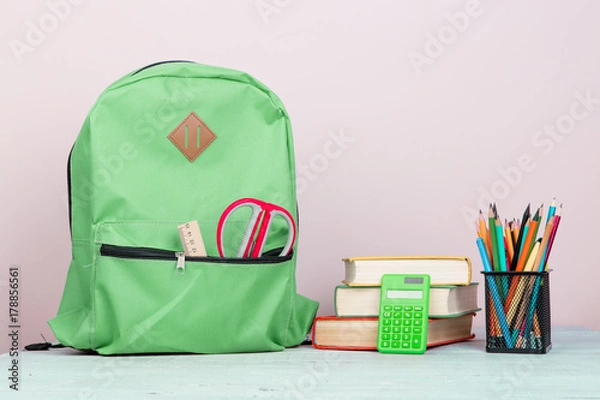 Fototapeta Green backpack and school supplies: notepad, books, scissors, pens, pencils, ruler, calculator is on a white wooden table