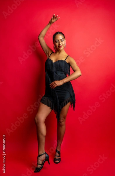 Fototapeta Woman in a black fringed dress dancing salsa on a vibrant red background