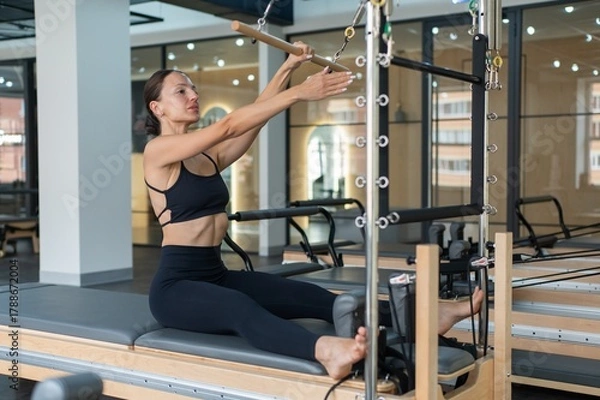 Obraz Caucasian woman doing exercises on reformer machine. 