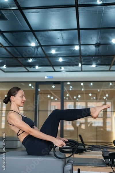 Obraz Caucasian woman doing exercises on reformer machine. 