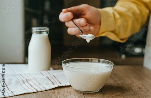 Fototapeta Close-up of male hand in yellow sleeve scooping yogurt from a bowl