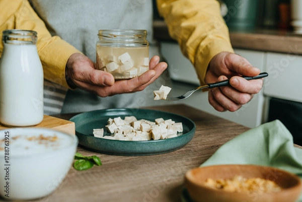 Fototapeta Males hands holding tofu on a fork over a jar