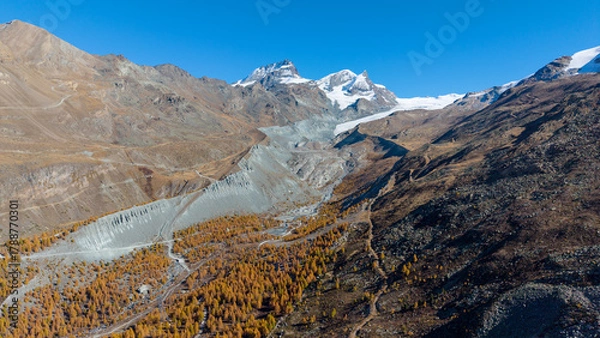 Fototapeta A drone view above Zermatt reveals the stunning Matterhorn region with its famous lakes, golden larches, and a deep blue autumn sky in perfect harmony.