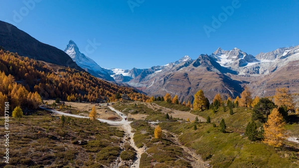 Fototapeta A drone view above Zermatt reveals the stunning Matterhorn region with its famous lakes, golden larches, and a deep blue autumn sky in perfect harmony.