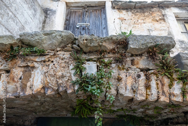 Fototapeta Weathered Stone Balcony With Plants And A Wooden Door Above A Crumbling Wall