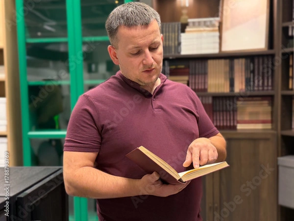 Fototapeta Man reading a book in a modern library