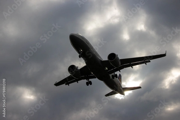 Obraz Airplane flying through dramatic cloudy sky, showcasing powerful engines and sleek design, symbolizing travel, adventure, and modern aviation technology