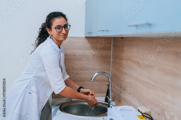 Fototapeta A doctor washing hands at a modern sink, ensuring hygiene and cleanliness in a clinical setting.