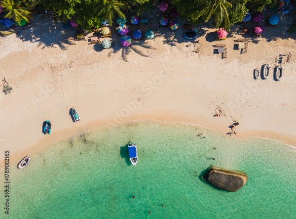 Fototapeta Stunning top-down aerial view of tropical Tanjung Tinggi beach in Belitung, Indonesia. Features clear turquoise water, giant granite boulders, boats, and colorful umbrellas.