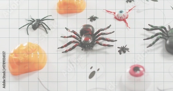 Obraz Sitting glossy black-and-red plastic spider on white grid mat at table, with pumpkins and eyeballs