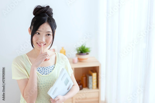 Obraz 体重計を持って指を立てるポーズをする女性