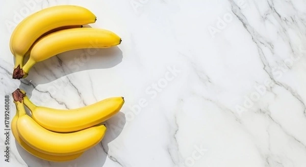 Obraz A still life of two bunches of yellow bananas on a white marble surface with soft shadows and bright lighting