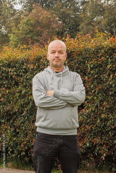 Obraz Serious bald man standing outdoors with arms crossed