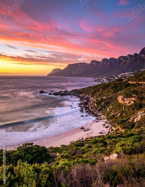 Fototapeta Coastal vista captured at dusk, revealing a long beach nestled between a rugged coastline and mountains under a vibrant, painted sky