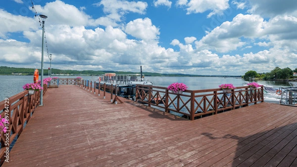 Obraz A wooden pier on Lake Żarnowieckie. Pink surfinias hang from the railing. A beautiful summer day. Nadole, Kashubia, Poland