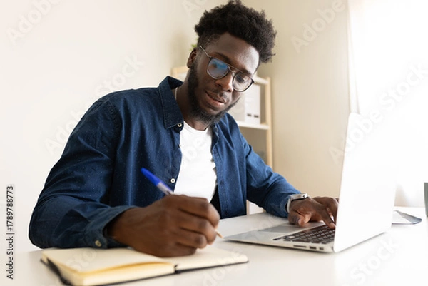 Obraz African American man working at home office using laptop.
