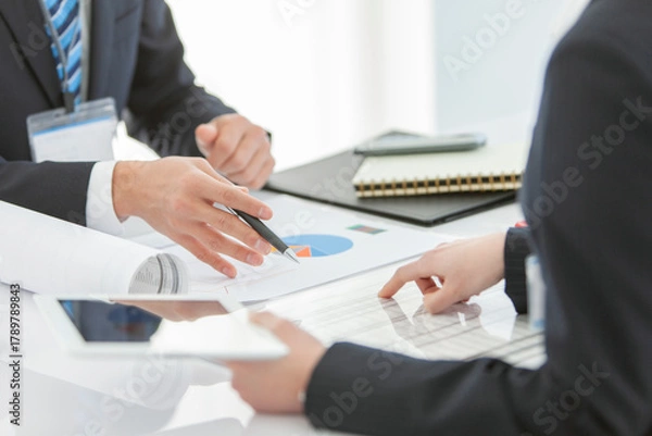 Obraz 資料を見せて打ち合わせをするビジネスマンとビジネスウーマン 