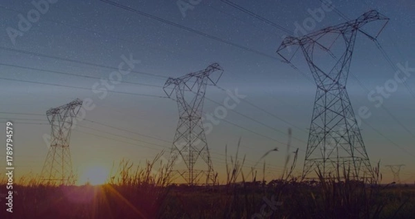 Obraz Silhouetting three high-voltage towers and power lines over rural field at sunset with tall grasses