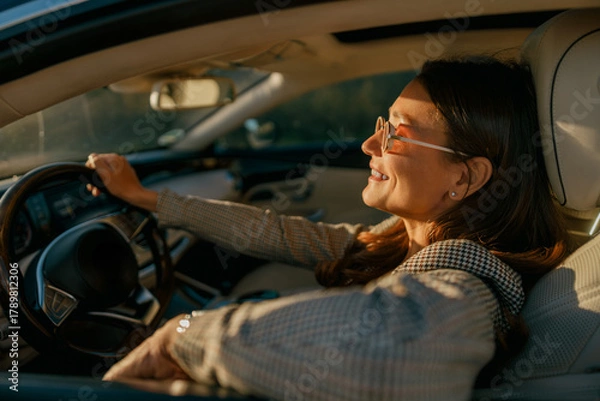 Fototapeta Woman enjoying sunlight and serene pause, eyes closed with relaxed posture while parked, warm glow and calm interior emphasize