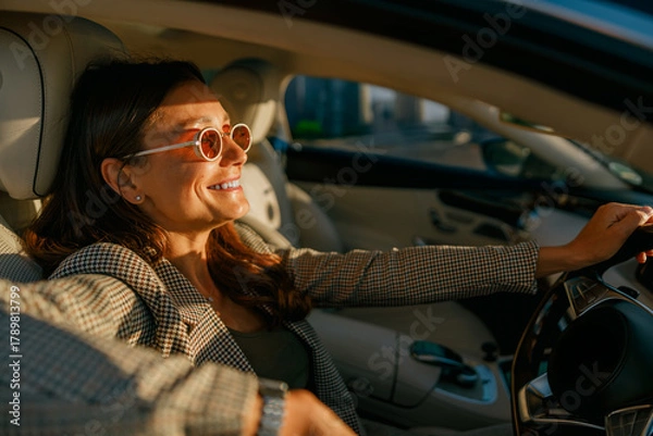 Fototapeta Woman poised at wheel in city, confident expression and sunglasses reflect determined morning commute, sleek interior and skyline