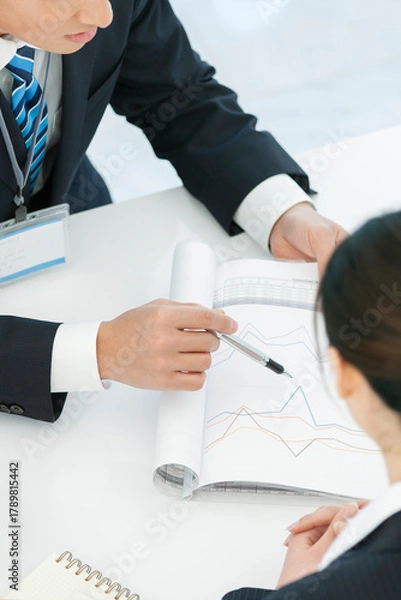 Obraz 資料を見せて打ち合わせをするビジネスマンとビジネスウーマン 