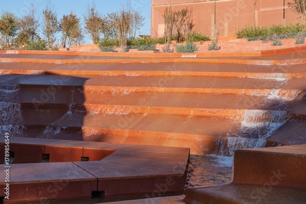 Fototapeta Modern cascading water fountain with terraced red-brown steps, creating serene and visually striking flow of water. Water amphitheater or canyon in Krasnodar's city park, or Galitsky Park.