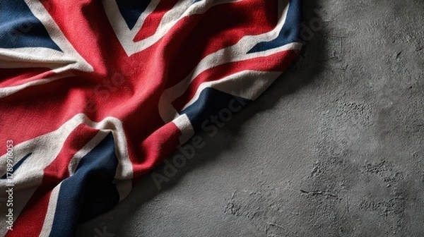Fototapeta United Kingdom flag lying flat on textured concrete floor, photographed from directly above. Fabric edges slightly curled, shadows
