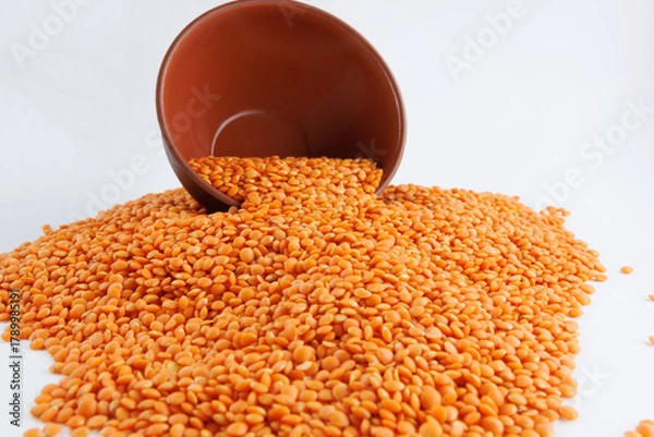 Fototapeta Red lentil background. Beautiful red lentils spill out of a clay cup.