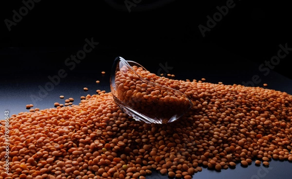 Fototapeta Red lentil background. Glass cup on a pile of red lentils on a black background.