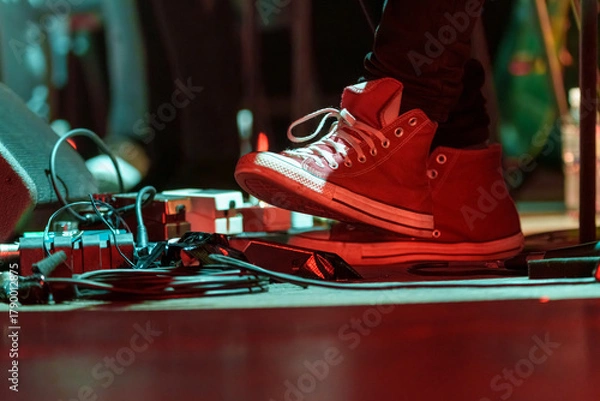 Fototapeta Closeup of a man’s feet pressing knobs on electric guitar pedals during a live performance, controlling sound effects and tone adjustments on stage