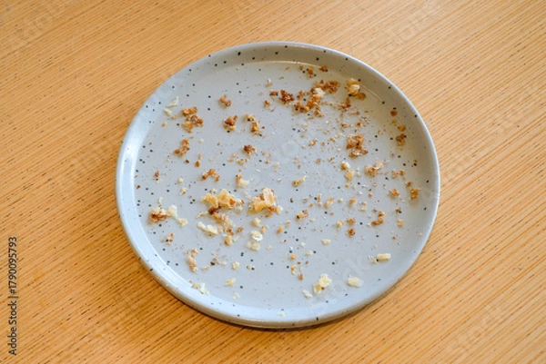Obraz Top view of an empty gray ceramic plate with bread crumbs and food remains on a wooden table in natural light. Perfect for lifestyle blogs, restaurant ads, or food background designs