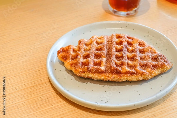 Obraz A crispy fish shaped waffle served on a light gray ceramic plate over a wooden table in natural light with a glass of single origin coffee. Perfect for restaurant, homemade bakery, or breakfast menu