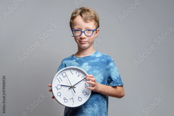 Fototapeta Smiling little boy in glasses holds clock in his hands