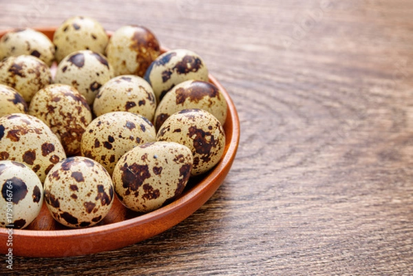 Fototapeta Closeup view of quail eggs in wooden plate on table